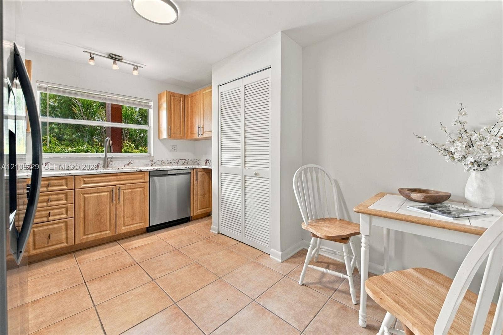 Kitchen featuring natural wood cabinetry, stone-finish countertops, stainless steel dishwasher, louvered-panel pantry door, and ceramic tile flooring