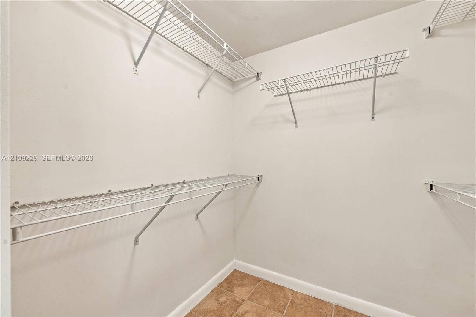 Storage area featuring white walls, tiled flooring, and multiple tiers of installed white wire shelving