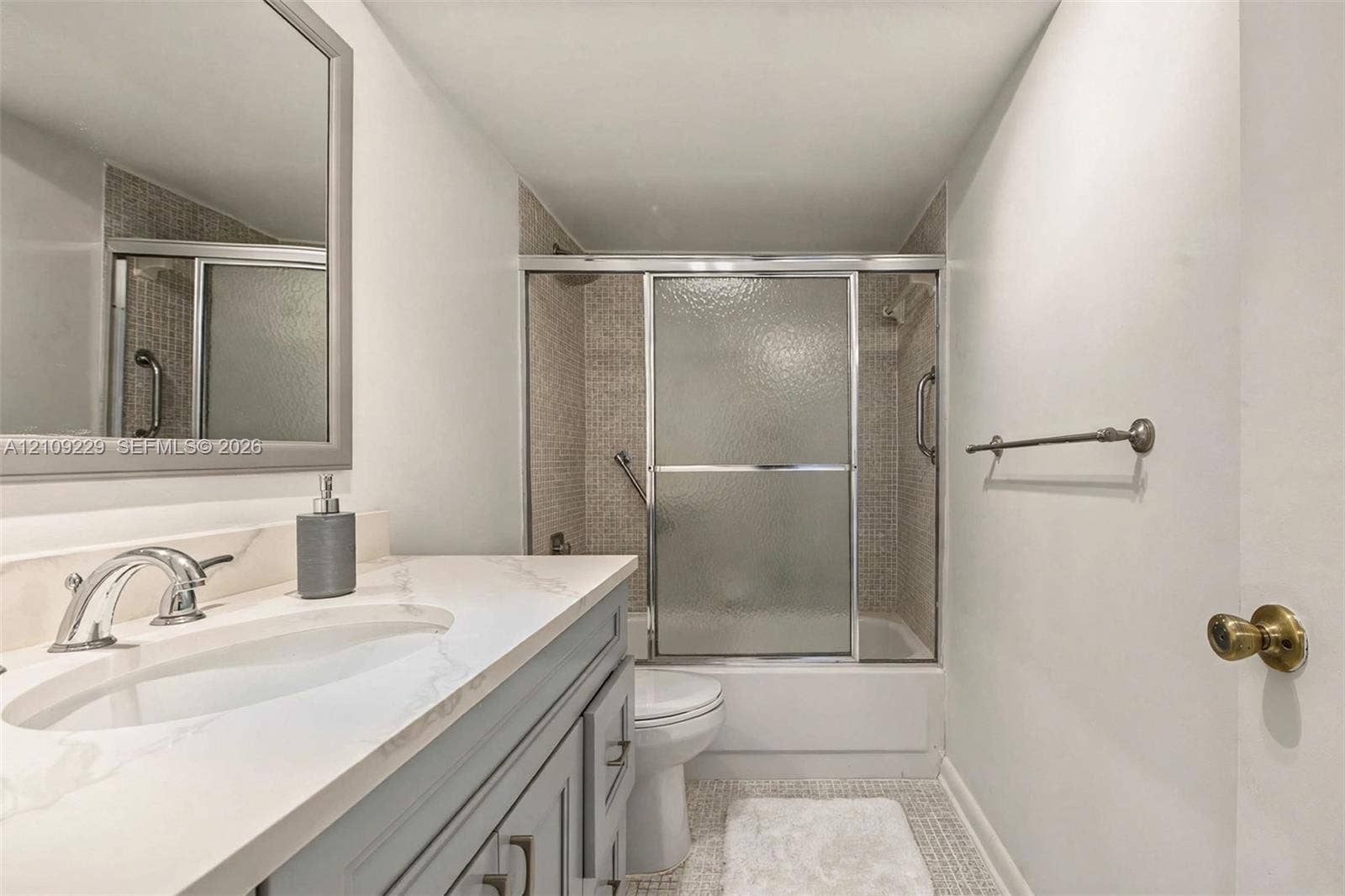 Bathroom featuring a gray vanity cabinet, white countertop with an integrated basin, chrome faucet, tiled shower surround, and sliding glass shower doors