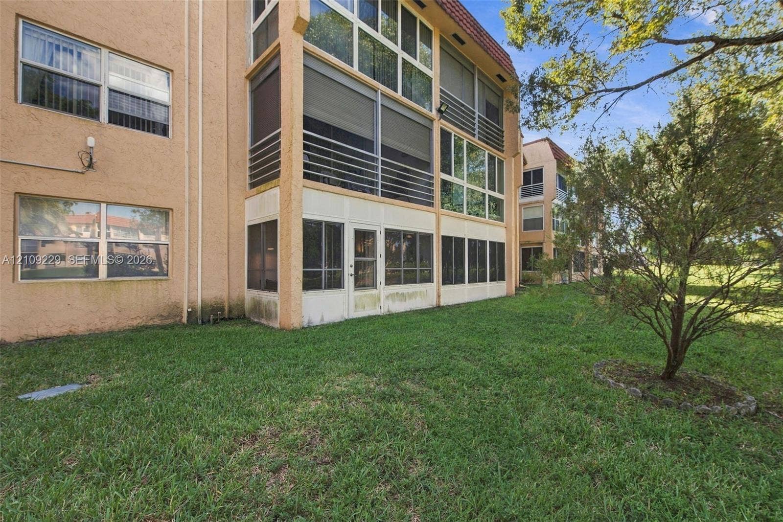 Multi-story stucco exterior featuring screened-in lanais with metal railings, expansive window banks, and surrounding landscaped grounds