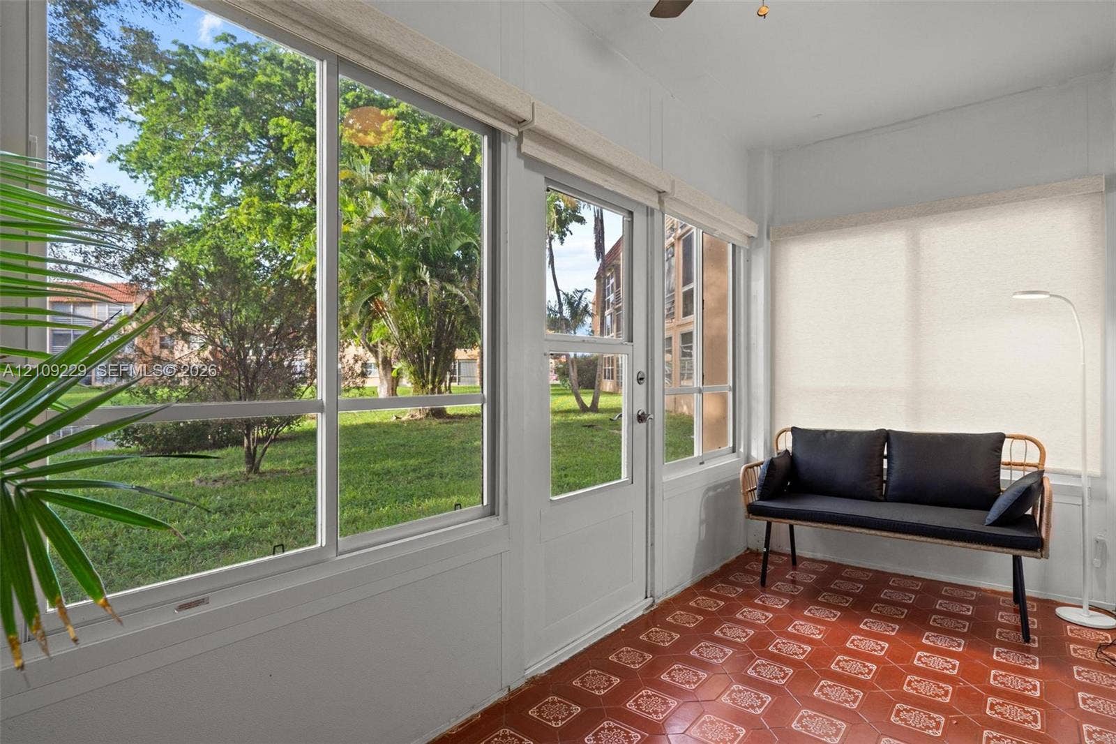 Enclosed sunroom featuring expansive windows, geometric-patterned tile flooring, a ceiling fan, and a glass-paneled entry door