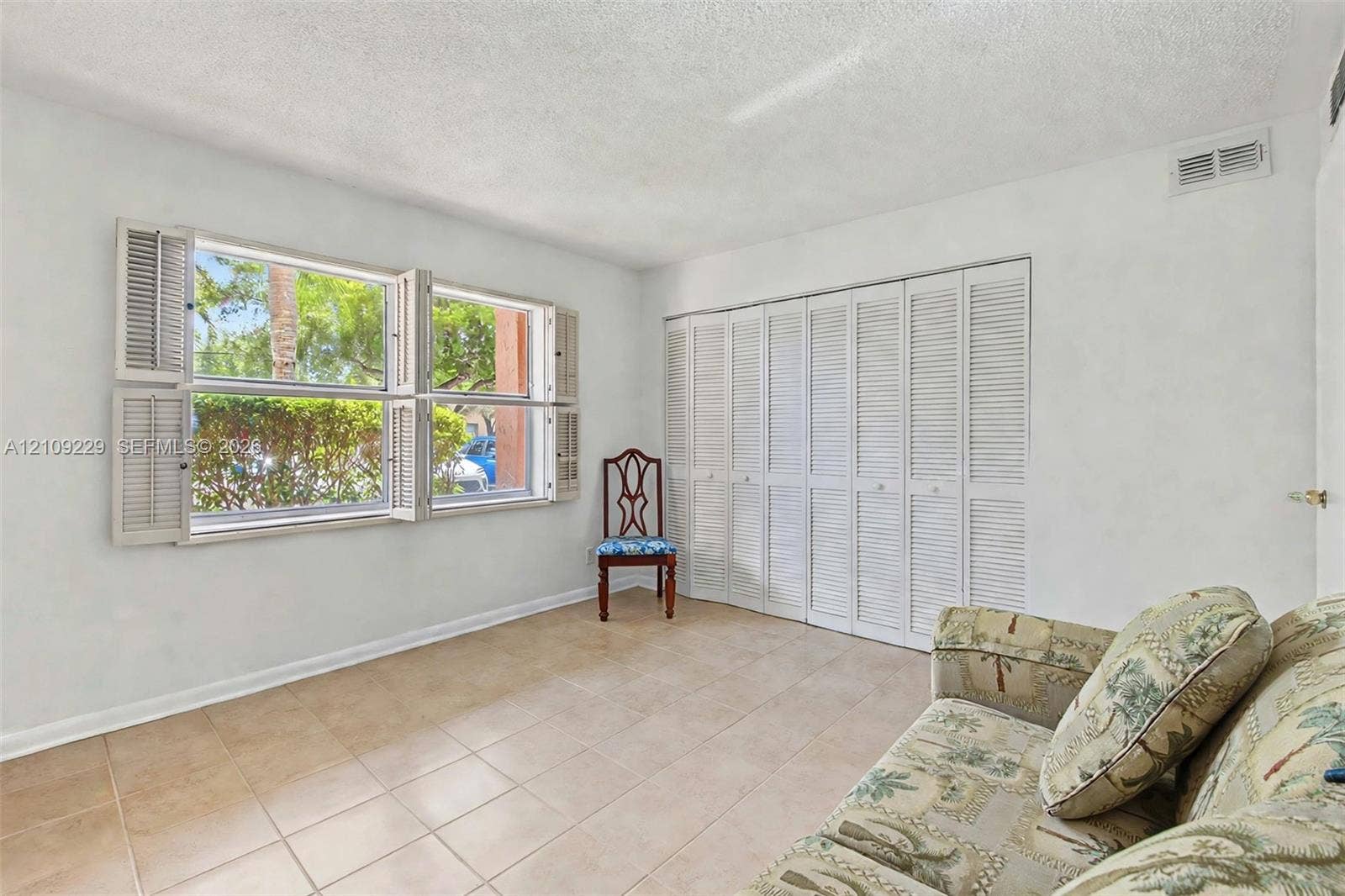 Room featuring tile flooring, white accordion-style closet doors, and windows equipped with louvered shutters