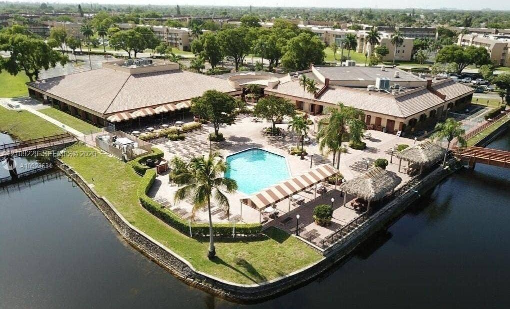 Waterfront community grounds featuring a central swimming pool, paved patio, palm trees, and covered cabanas