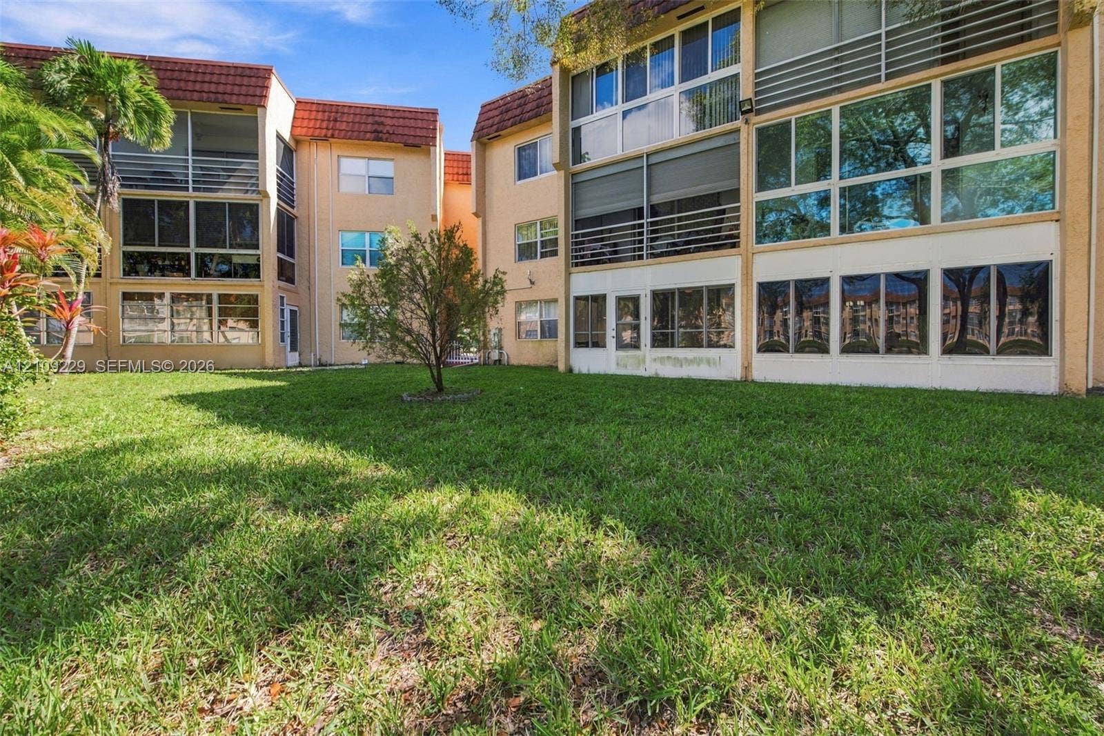 Multi-story building exterior featuring a tile roof, expansive multi-pane windows, and screened-in balcony enclosures overlooking a landscaped lawn area