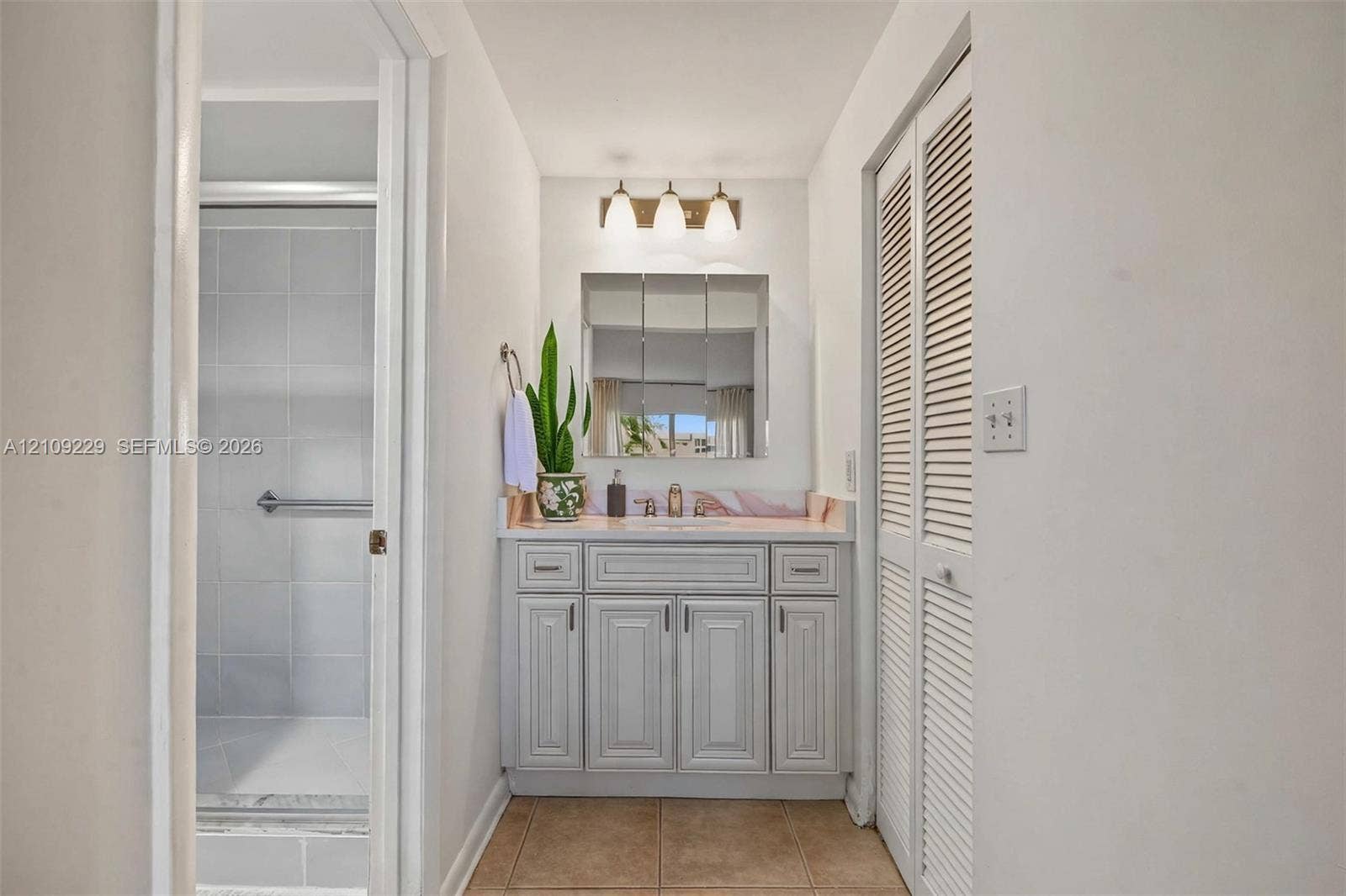 Bathroom featuring a vanity with raised-panel cabinetry, tile countertop, triple-light fixture, medicine cabinet, and bifold louvered closet doors