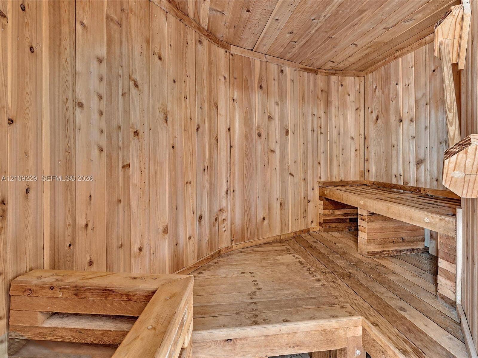 Sauna featuring vertical wood wall paneling, tiered wood bench seating, and wood flooring