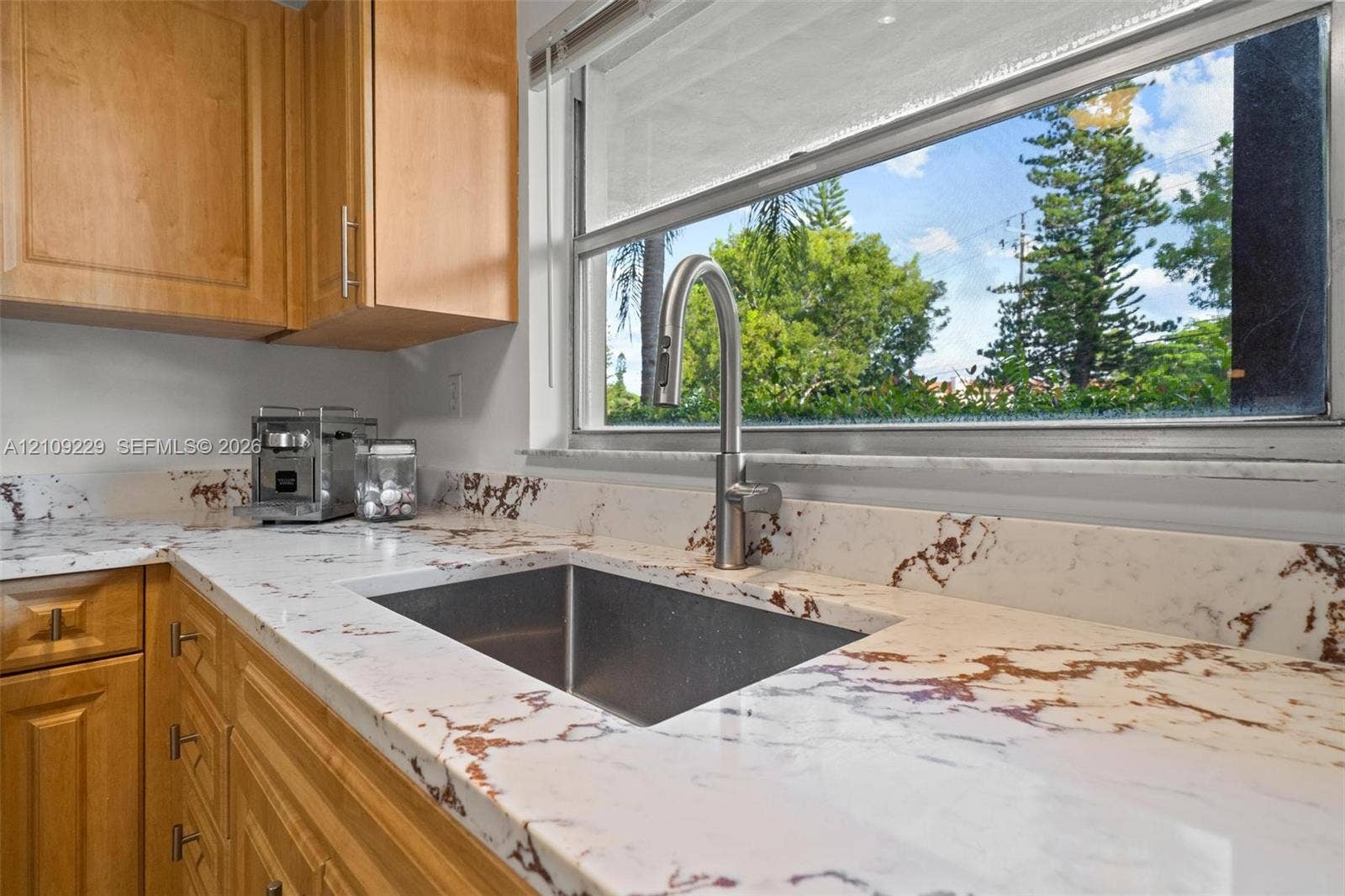 Kitchen featuring natural wood-tone cabinetry, stone-patterned countertops, a stainless steel undermount sink, and a gooseneck pull-down faucet
