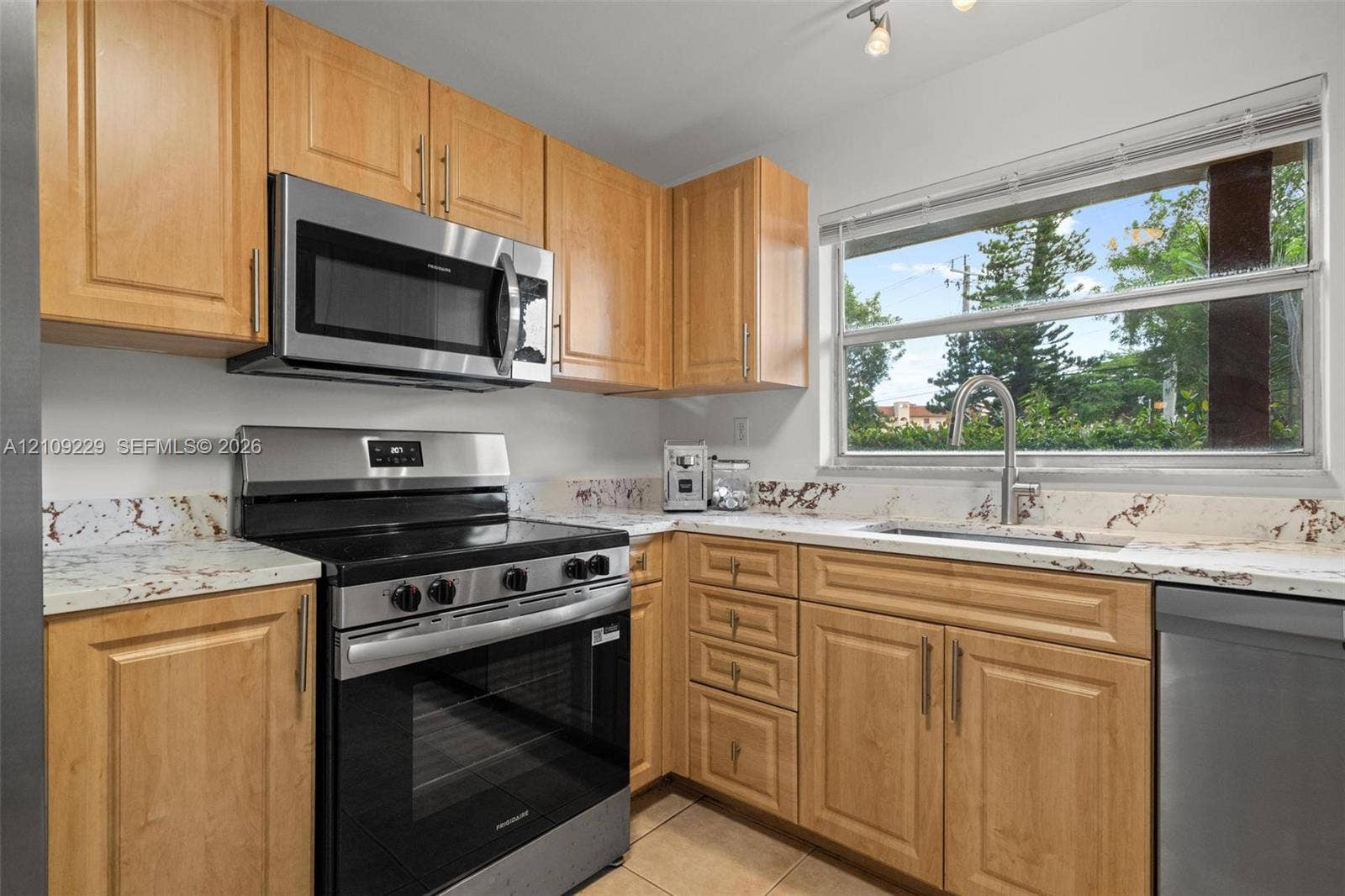 Kitchen featuring light-finish cabinetry, stone-patterned countertops, stainless steel appliances, and a polished metal faucet
