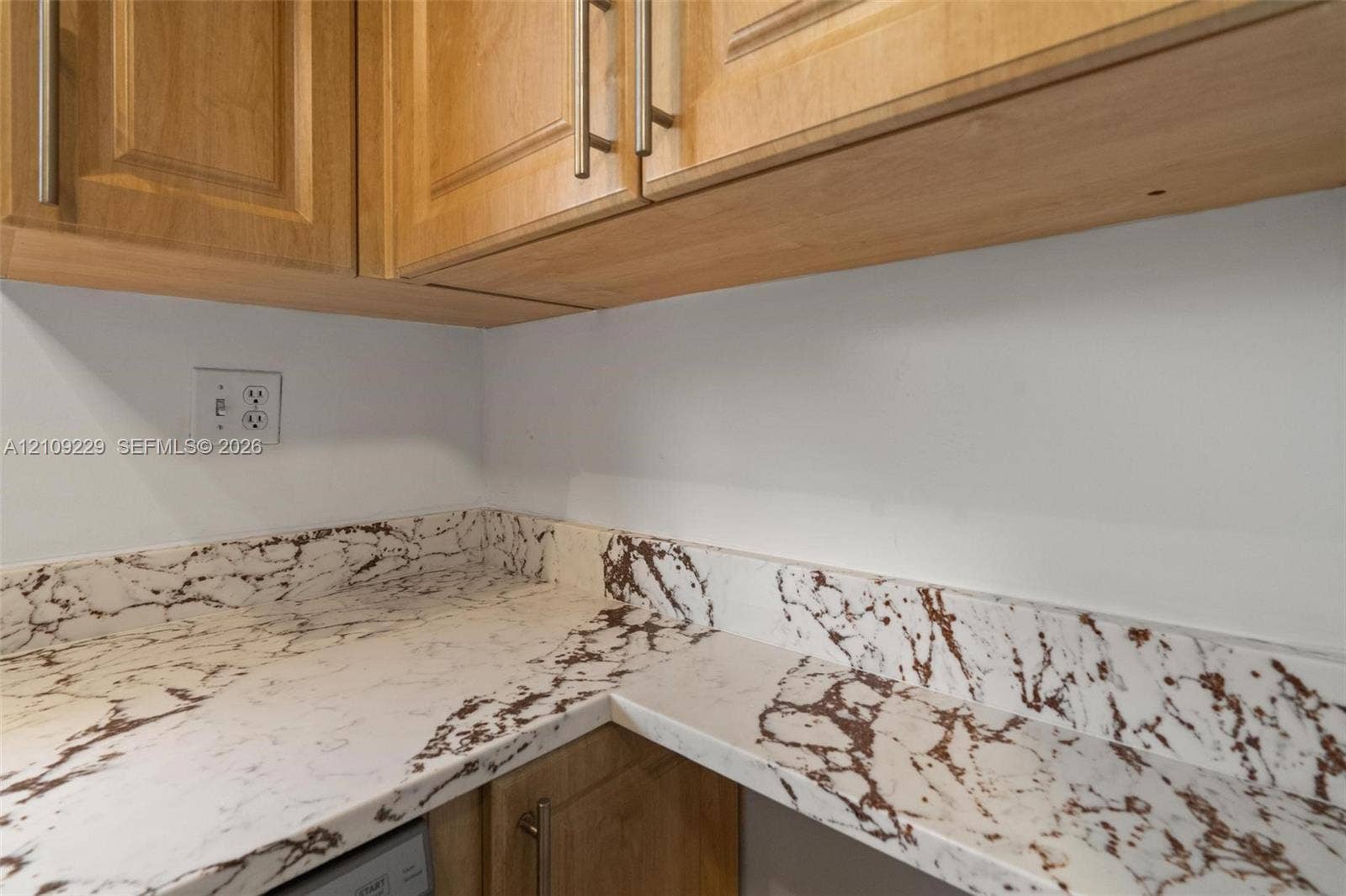Light-toned wood cabinetry with vertical bar pulls and stone-patterned countertops featuring a matching integrated backsplash
