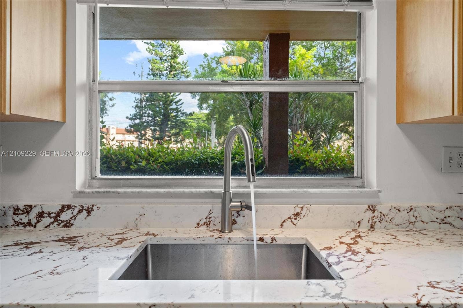 Stainless steel under-mount sink featuring a high-arc pull-down faucet, stone-finish countertops with integrated backsplash, and light-tone wood-finish cabinetry