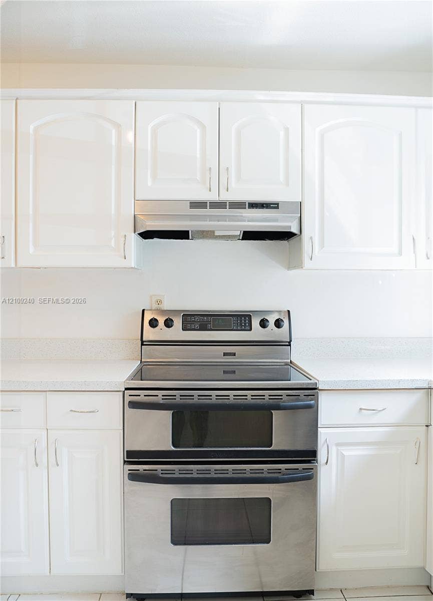 21115 SW 125th Ct Road, Miami, Miami, FL 33177 White cabinetry featuring arched-panel doors, stainless steel double-oven range, integrated stainless steel range hood, and solid-surface countertops