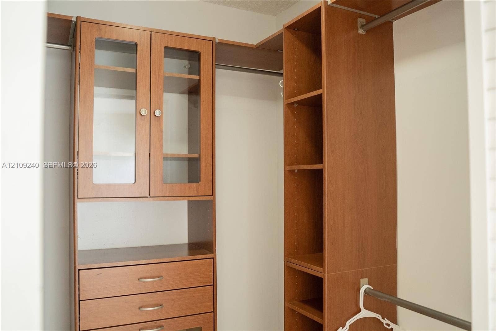 21115 SW 125th Ct Road, Miami, Miami, FL 33177 Custom wood-finish closet storage system featuring built-in cabinetry, glass-front upper doors, three drawers with metallic pulls, adjustable shelving, and integrated garment rods