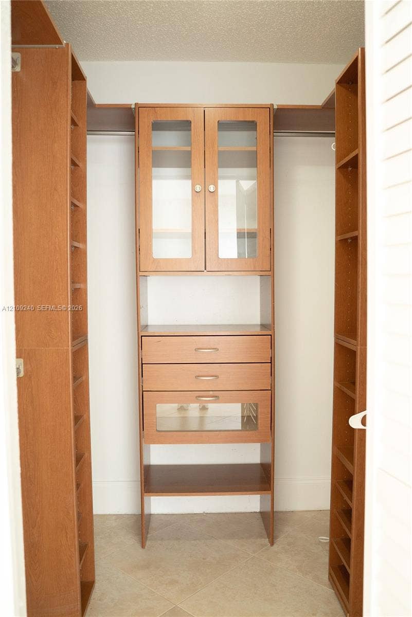 21115 SW 125th Ct Road, Miami, Miami, FL 33177 Custom built-in wood-finish cabinetry featuring glass-panel cabinet doors, three integrated drawers, open shelving, and hanging rods