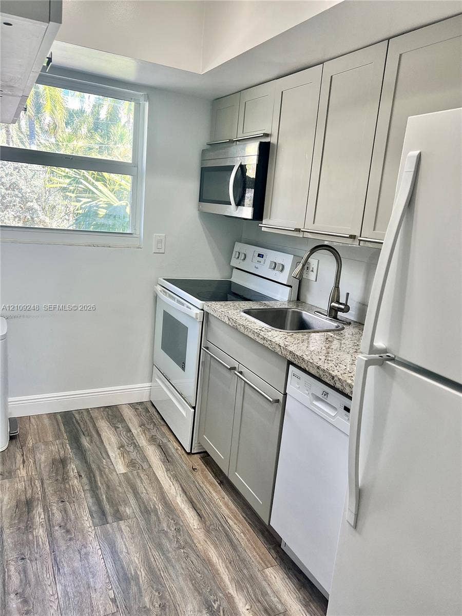 Kitchen featuring shaker-style cabinetry, stone-finish countertops, stainless steel undermount sink with gooseneck faucet, built-in stainless steel microwave, and wood-finish flooring