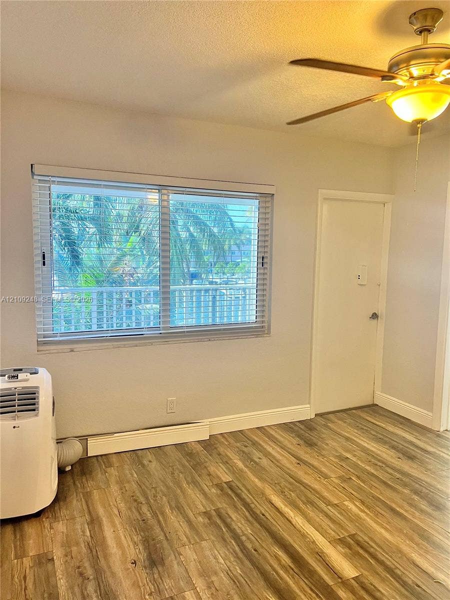 Interior space featuring wood-finish flooring, a ceiling fan with integrated lighting, and a large window equipped with horizontal blinds