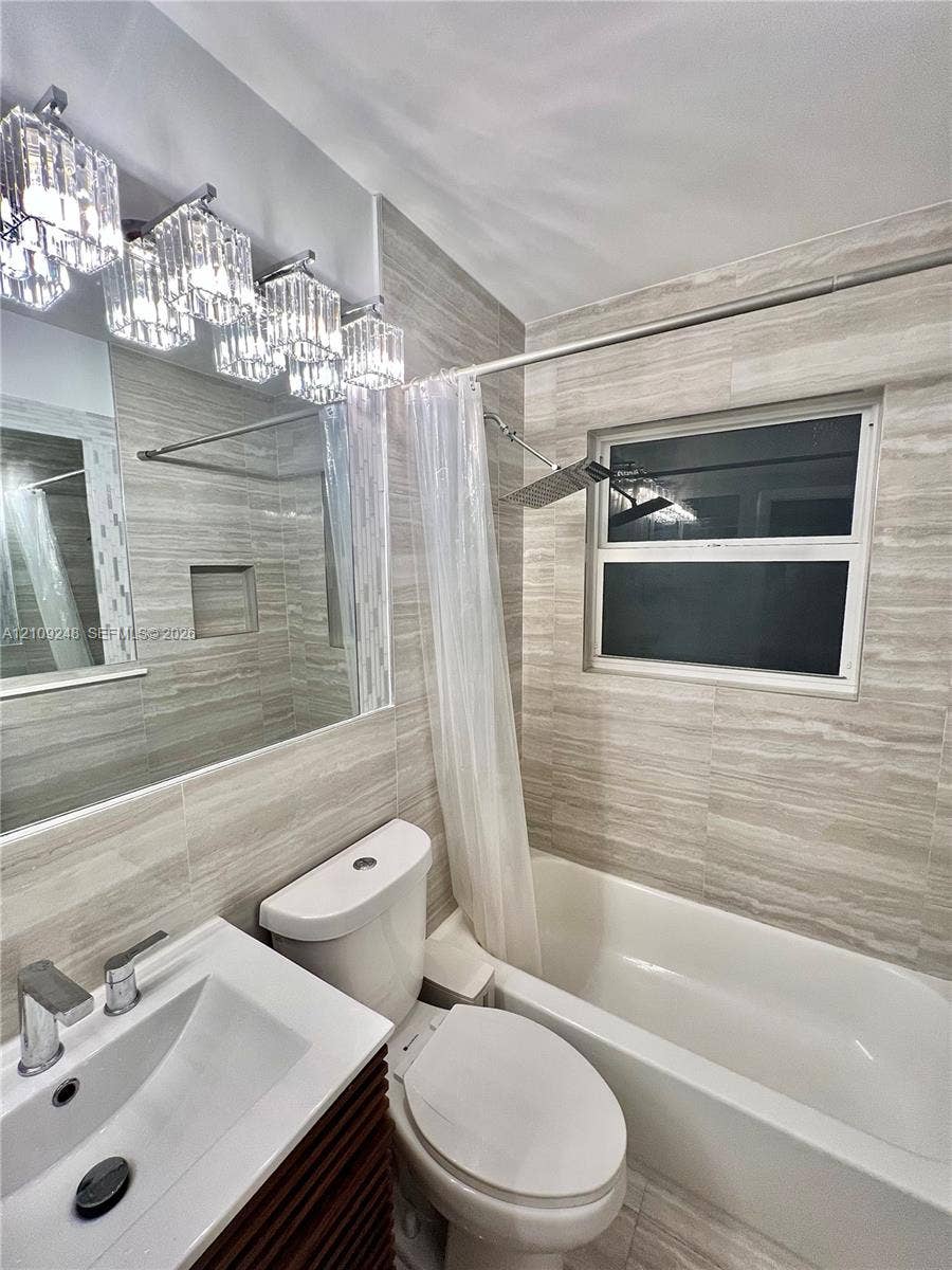 Full-wall neutral stone-look tiling, multi-light glass vanity fixture, integrated shower niche, rectangular vessel sink with chrome faucet, and overhead rainfall shower head