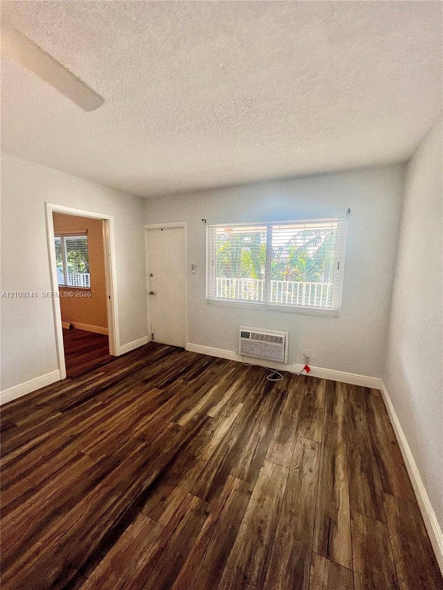 Room featuring wood-finish flooring, a multi-pane window, and a built-in wall air conditioning unit
