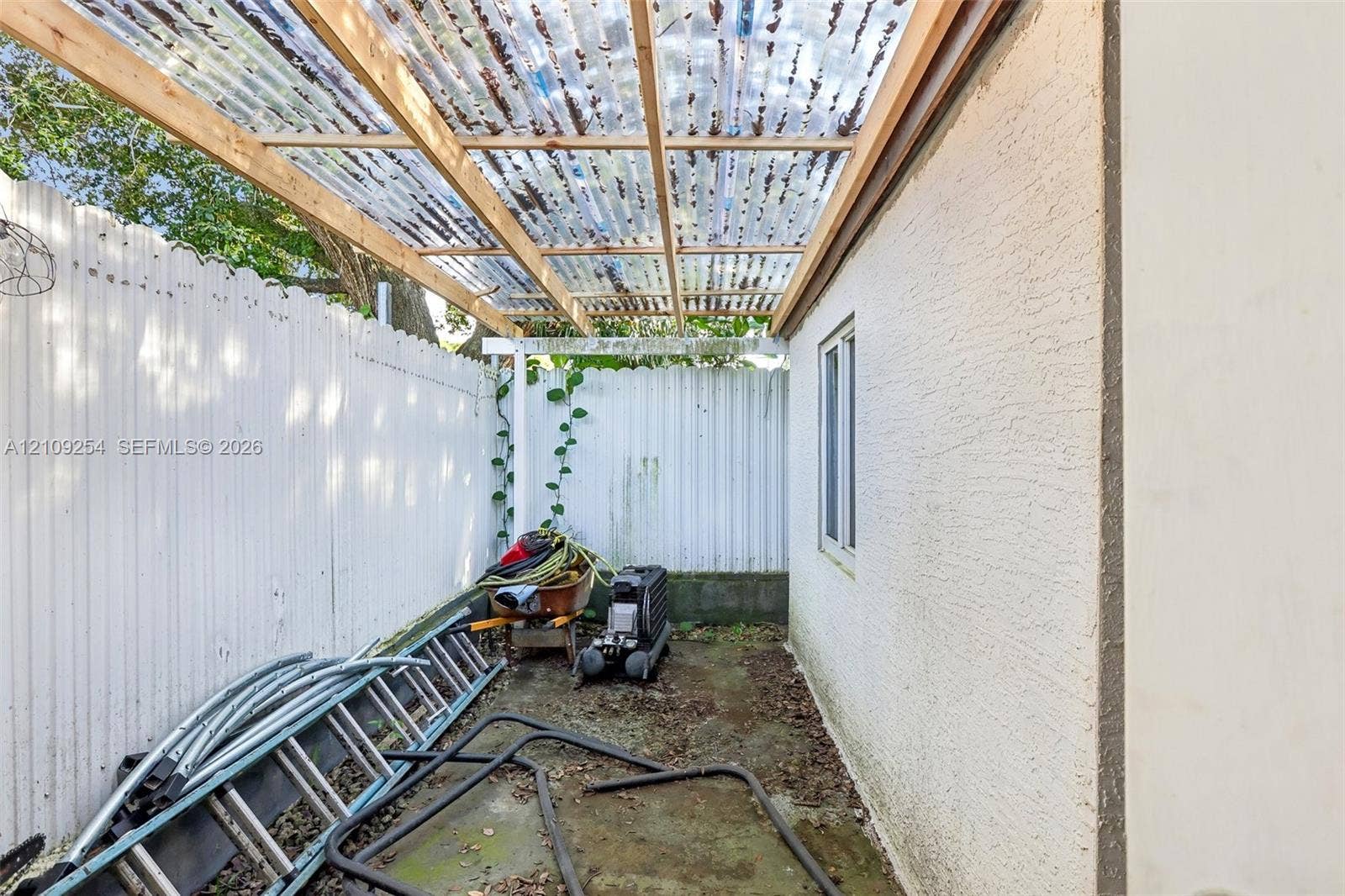 21342 NW 40th Cir Court, Miami Gardens, FL 33055 Side patio featuring a corrugated translucent roof, wood framing, stucco exterior wall, and white privacy fencing