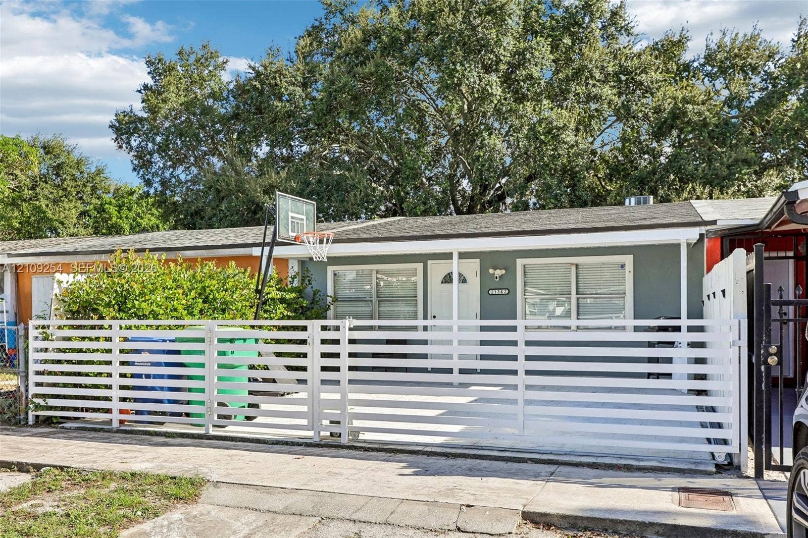 21342 NW 40th Cir Court, Miami Gardens, FL 33055 Single-story exterior featuring a horizontal slat privacy fence, concrete paved front area, and mature canopy trees