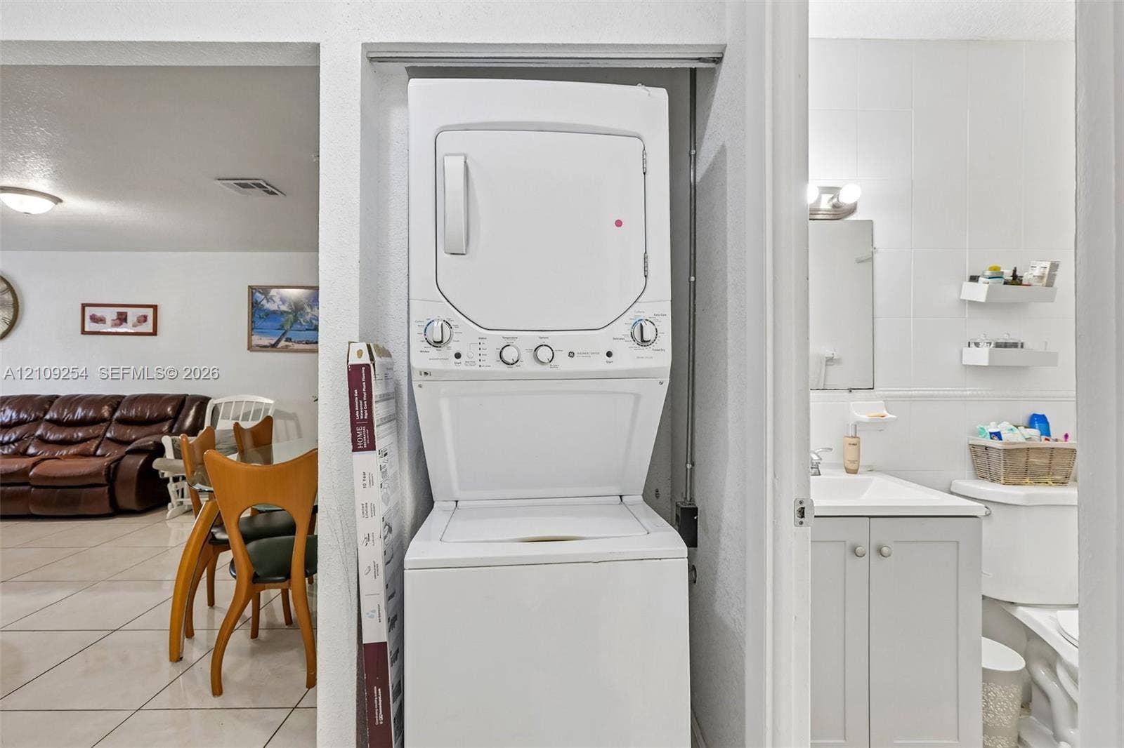21342 NW 40th Cir Court, Miami Gardens, FL 33055 Laundry closet featuring a white stacked washer and dryer unit, cabinet vanity with a rectangular sink, wall-mounted shelving, and tile flooring