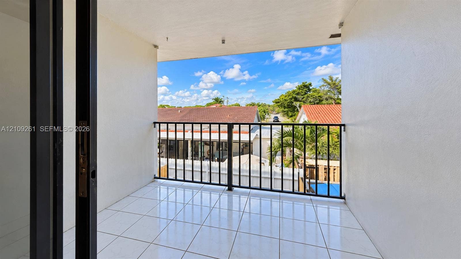 Covered balcony featuring white tile flooring, a black metal railing, and high-contrast smooth wall finishes