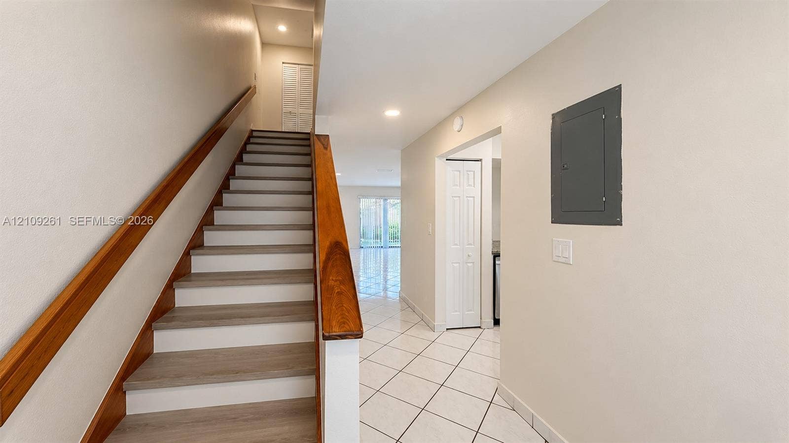 Staircase featuring wood-finish treads and a natural wood handrail, complemented by ceramic tile flooring and recessed lighting