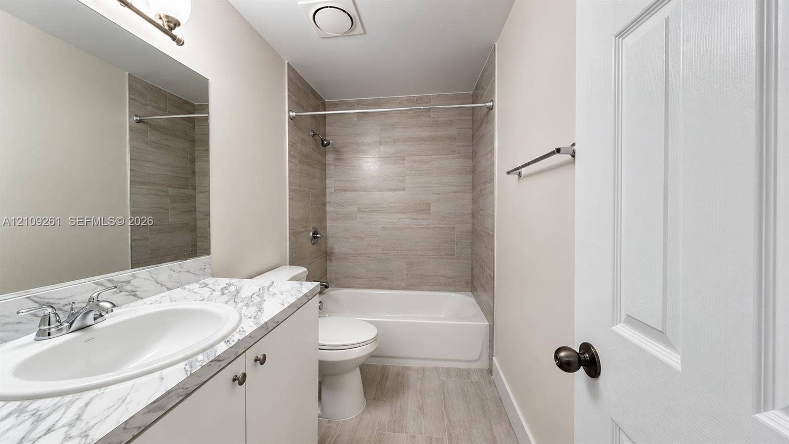 Full bathroom featuring a vanity with a stone-patterned countertop, an integrated sink, a bathtub with a tiled surround, and wood-finish tile flooring