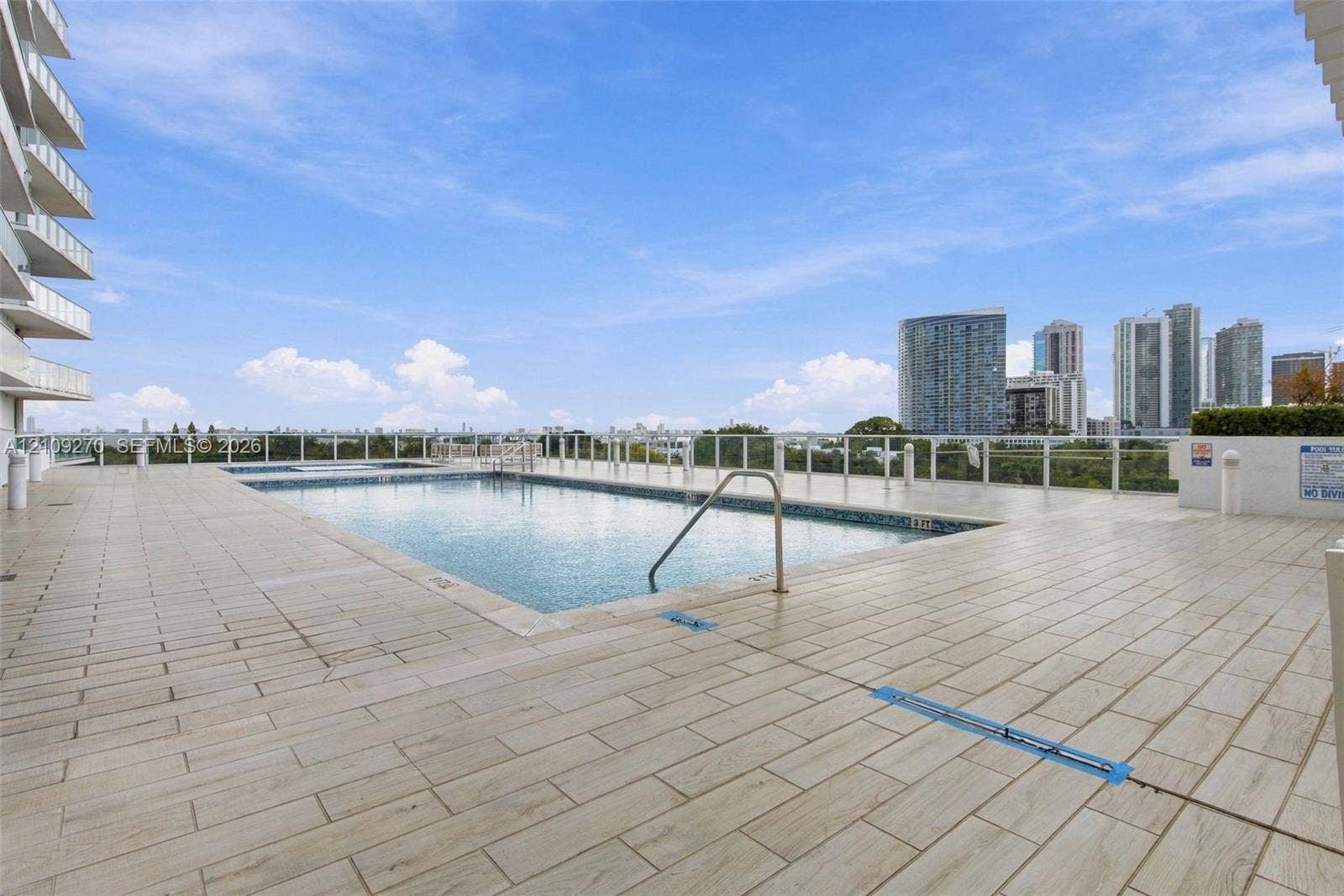 Rooftop swimming pool featuring tiled decking, metal perimeter railings, and a horizontal cityscape backdrop