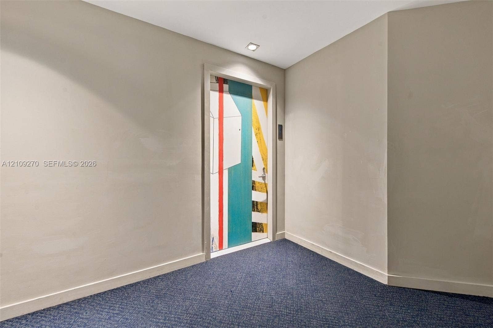 Neutral wall finishes, recessed ceiling lighting, and blue textured carpeting featuring a door with a custom geometric, multi-color graphic finish