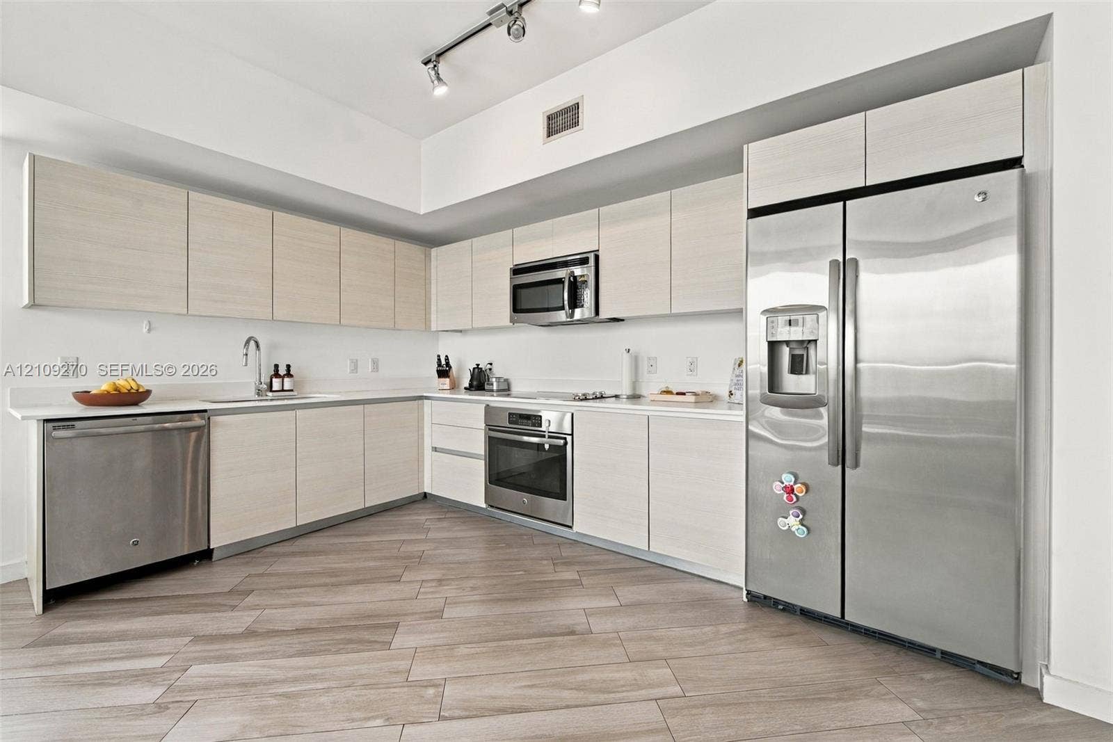 Kitchen featuring flat-panel cabinetry, light-toned countertops, stainless steel appliances, and plank-style flooring with integrated track lighting