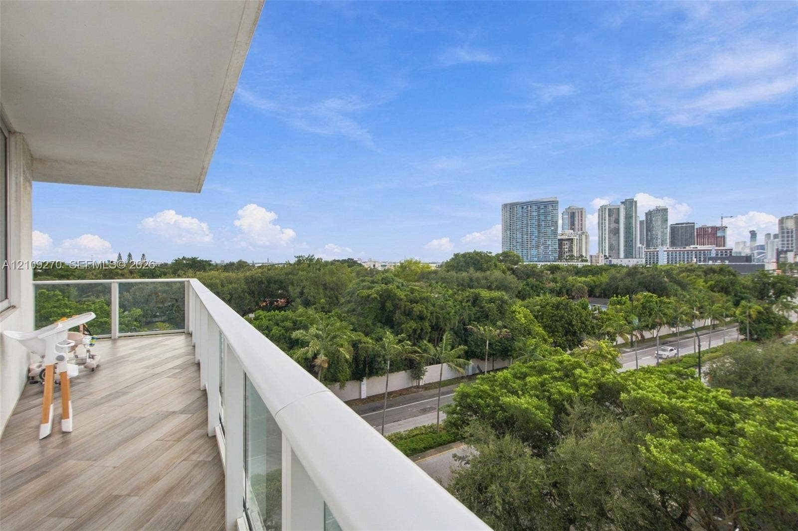 Private balcony with wood-finish flooring, glass railing, and expansive city skyline backdrop