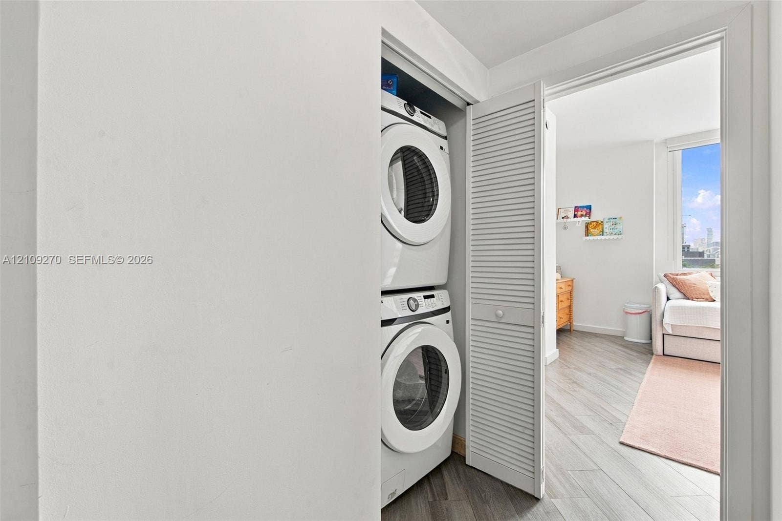 Laundry closet featuring a stackable washer and dryer unit enclosed by white louvered bi-fold doors