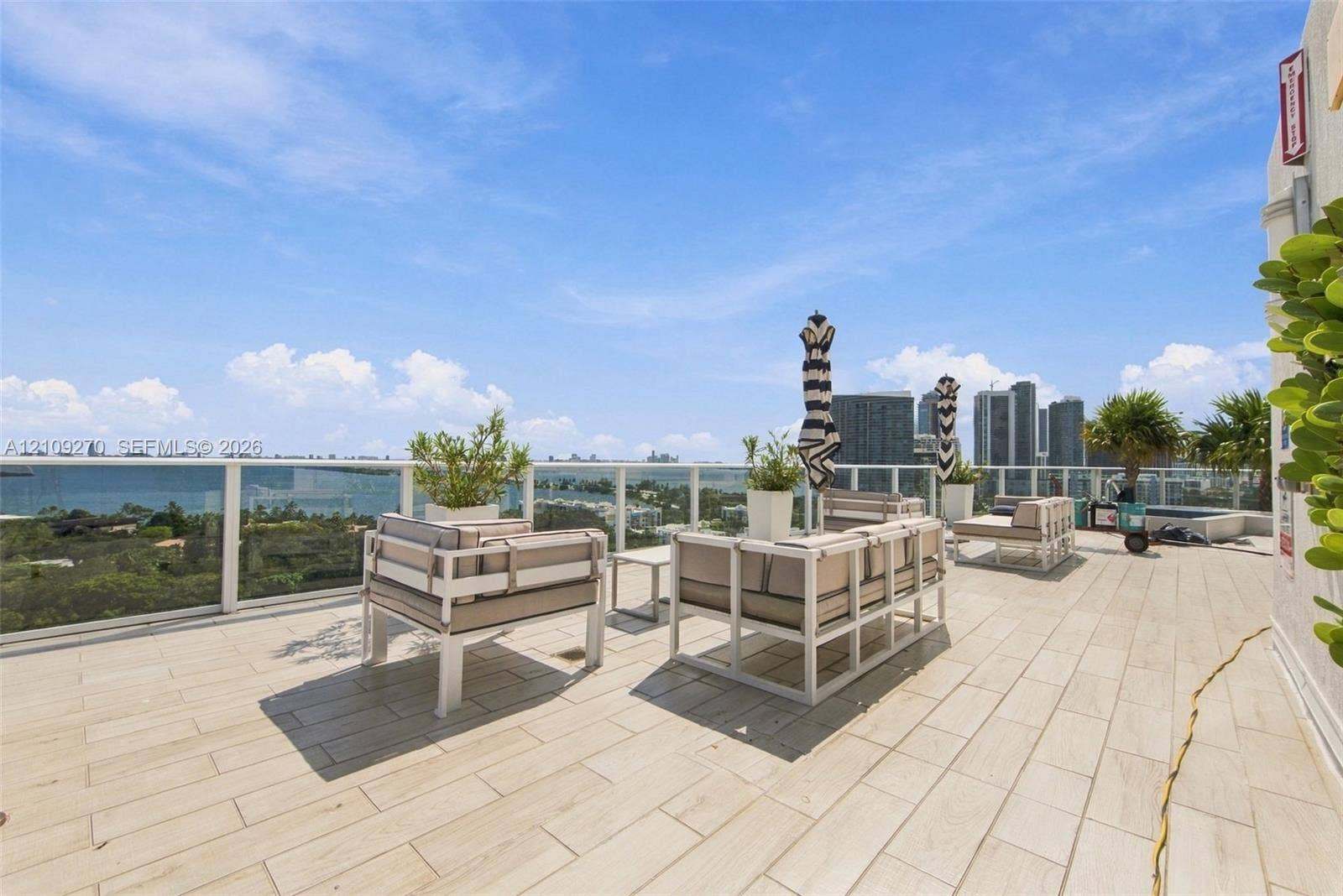 Expansive outdoor terrace featuring light-toned tile flooring, a glass panel railing, and a cityscape and water backdrop