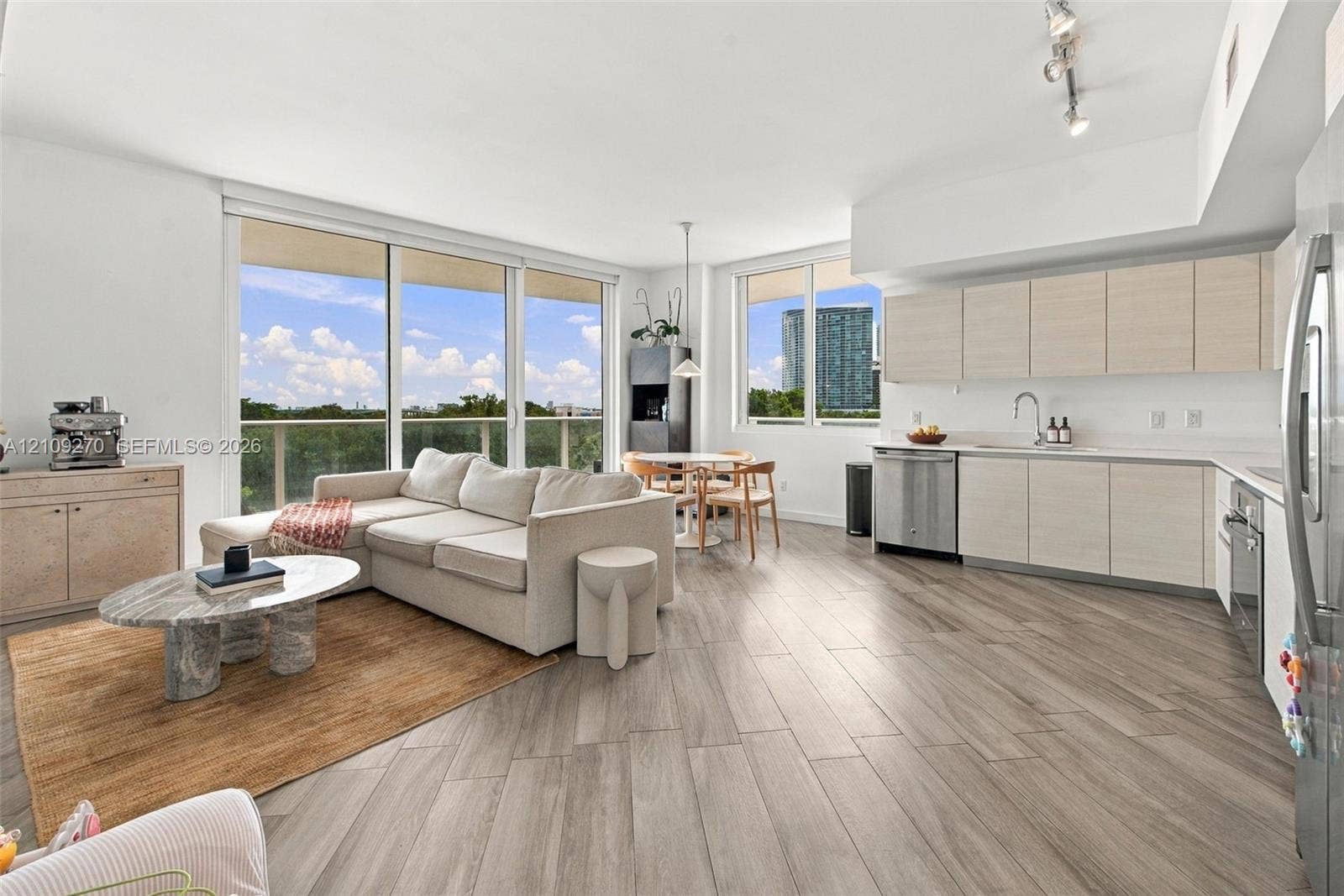 Open-concept main living area featuring wood-finish flooring, floor-to-ceiling glass sliding doors, flat-panel cabinetry, stainless steel appliances, and track lighting