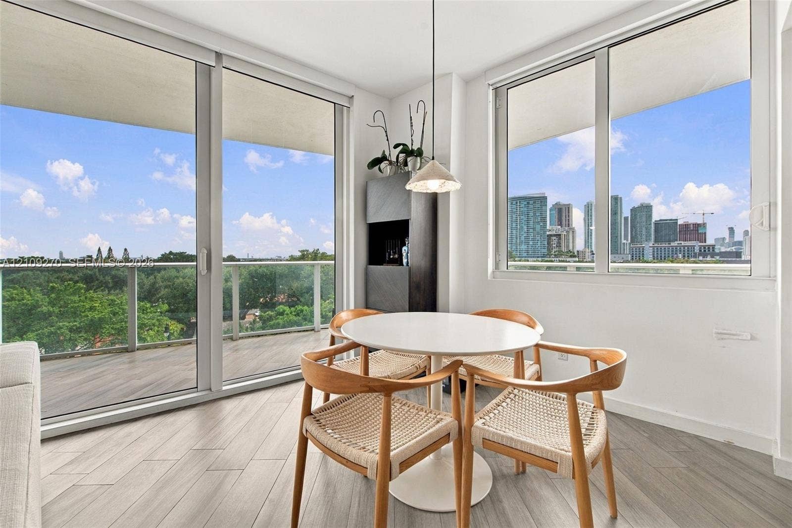 Floor-to-ceiling windows, wood-finish tile flooring, recessed balcony with glass railing, and a pendant light fixture