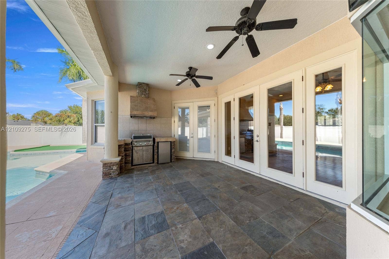 1035 SW 33rd Place, Ocala, FL 34471 Covered patio featuring stone-tile flooring, built-in outdoor kitchen with stainless steel grill, recessed ceiling lighting, dual overhead fans, and multi-panel glass entry doors