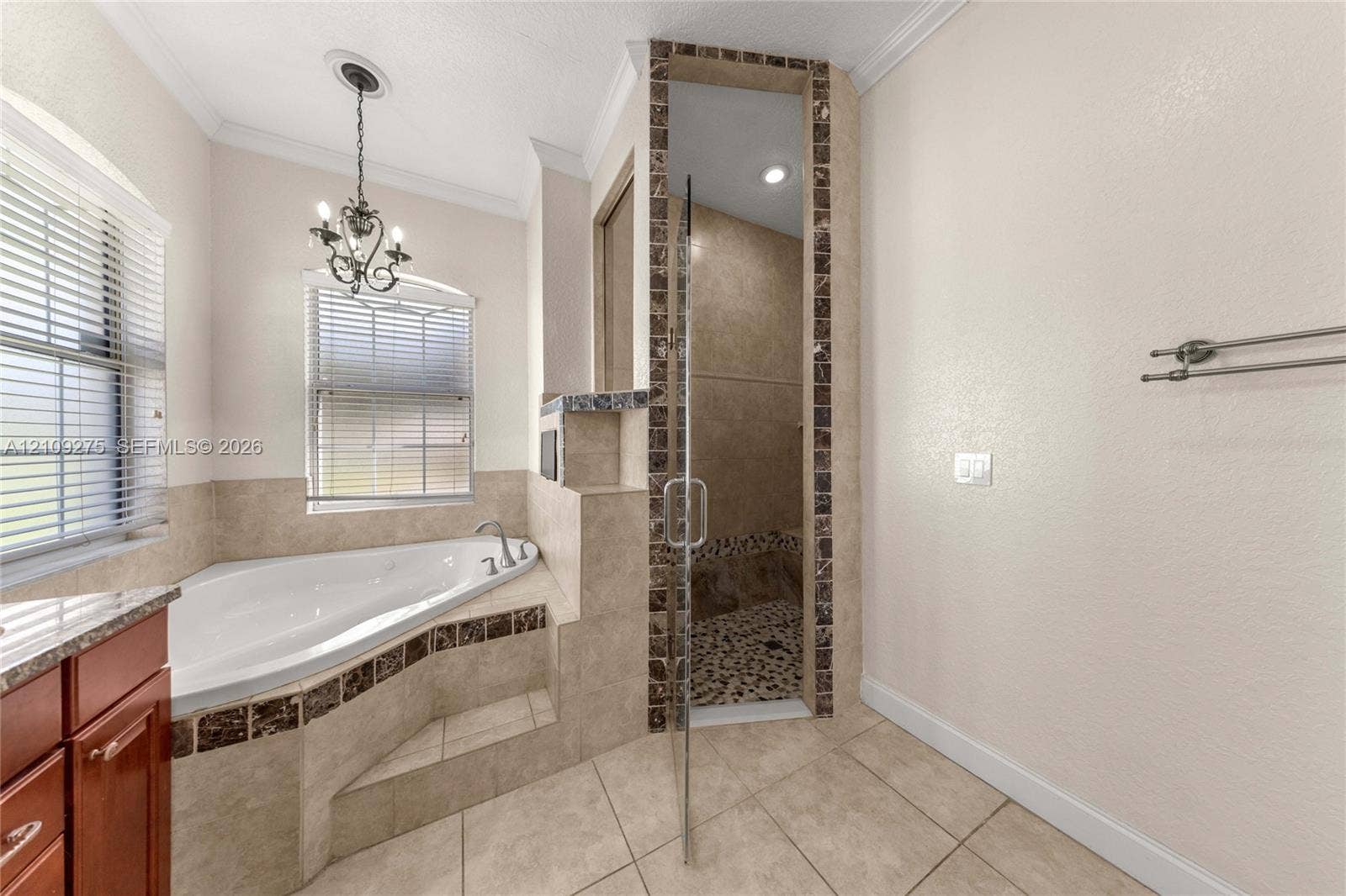 1035 SW 33rd Place, Ocala, FL 34471 Corner jetted soaking tub featuring decorative tile accents, glass-enclosed shower with stone tile flooring, crown molding, and metal chandelier fixture
