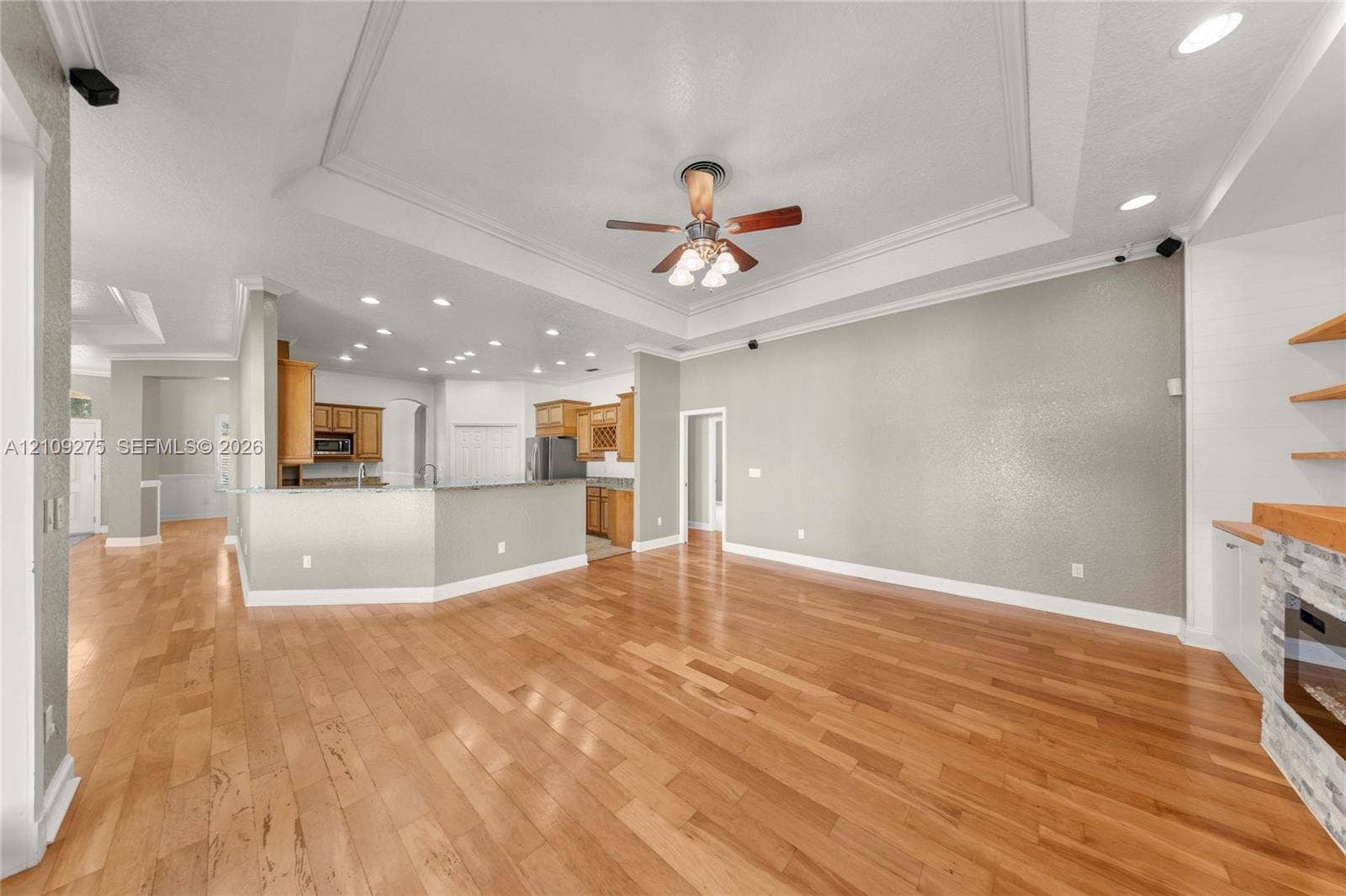 1035 SW 33rd Place, Ocala, FL 34471 Open floor plan featuring a tray ceiling, recessed lighting, wood-finish flooring, a kitchen peninsula, and a stone-accented fireplace