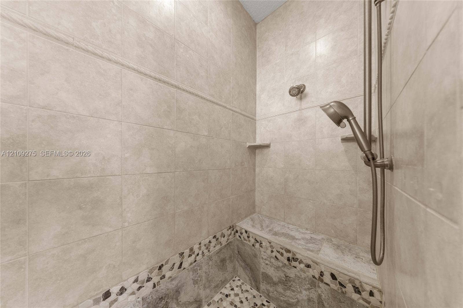1035 SW 33rd Place, Ocala, FL 34471 Walk-in shower featuring floor-to-ceiling tile, decorative stone inlay, a built-in stone bench, and an adjustable handheld showerhead