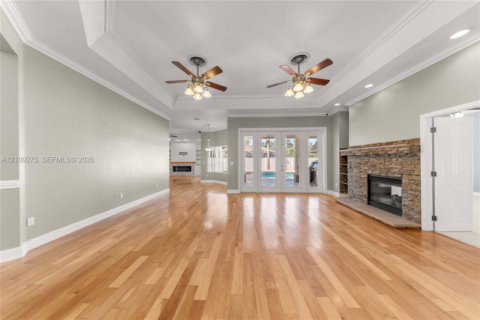 1035 SW 33rd Place, Ocala, FL 34471 Spacious living area featuring wood-finish flooring, tray ceilings with dual ceiling fans, a stacked-stone fireplace, and multi-panel glass doors