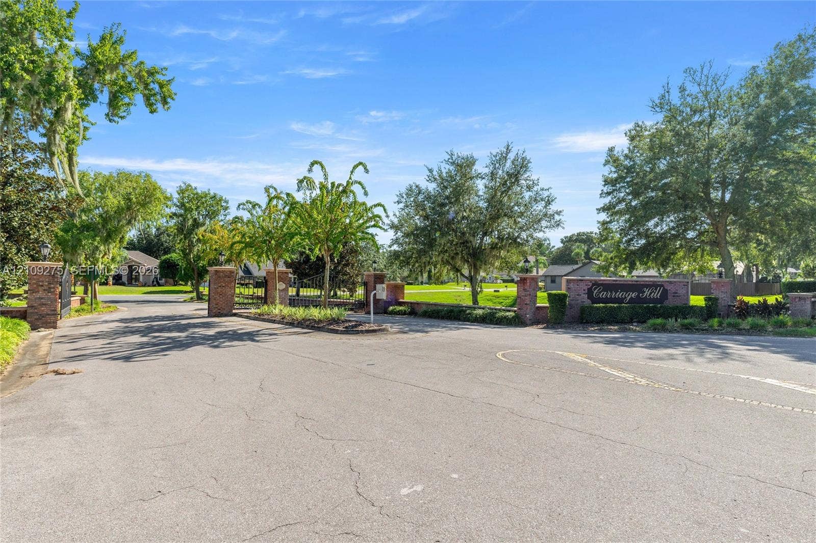 1035 SW 33rd Place, Ocala, FL 34471 Entryway featuring brick masonry pillars, ornamental metal gate, paved access road, and mature landscaping