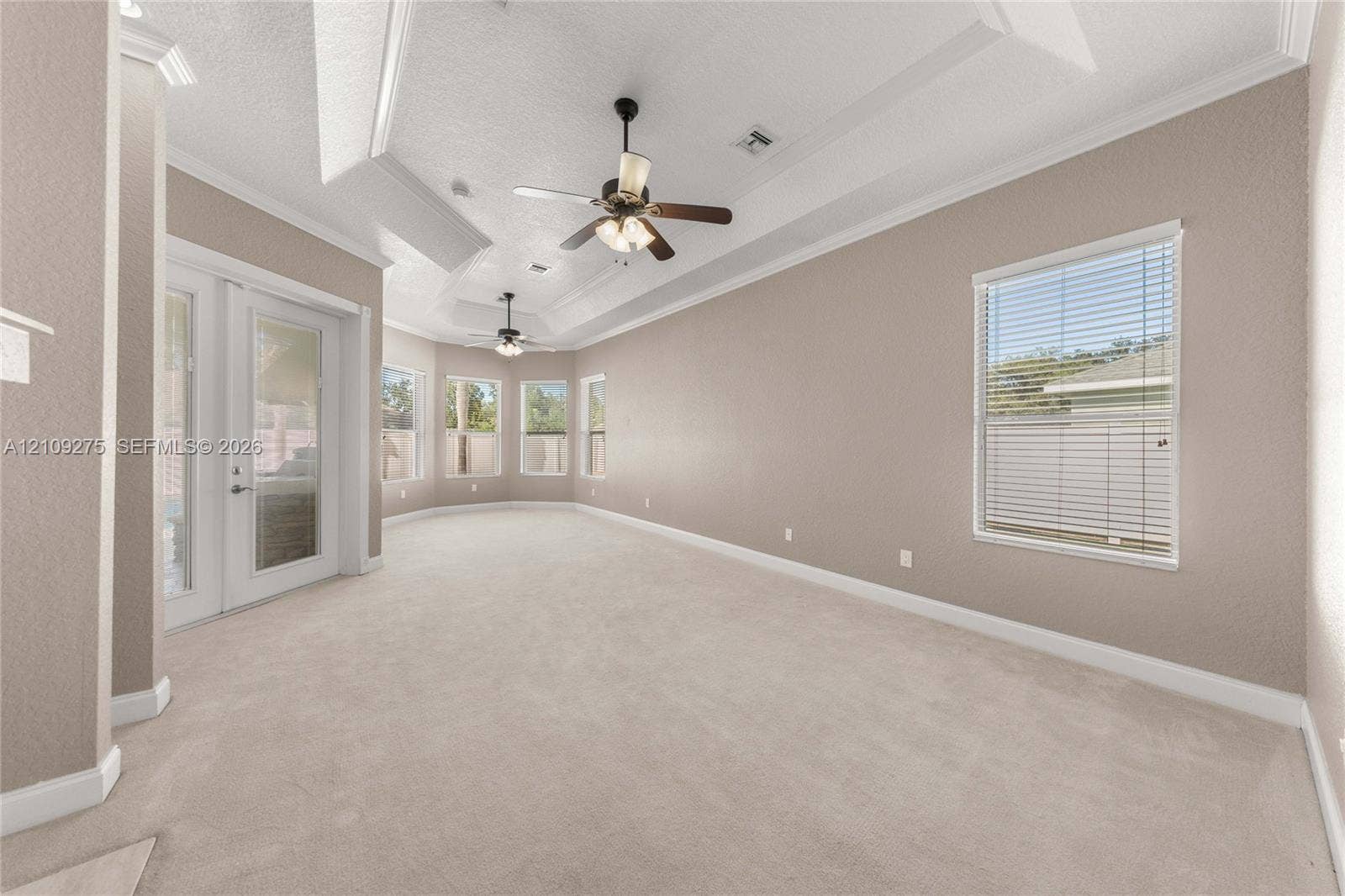 1035 SW 33rd Place, Ocala, FL 34471 Spacious room featuring a tray ceiling, dual ceiling fans with integrated lighting, neutral wall-to-wall carpeting, crown molding, and glass panel doors