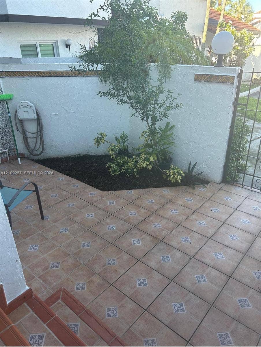 Enclosed courtyard featuring patterned ceramic tile flooring, a structured garden bed, white masonry perimeter walls, and iron gate access