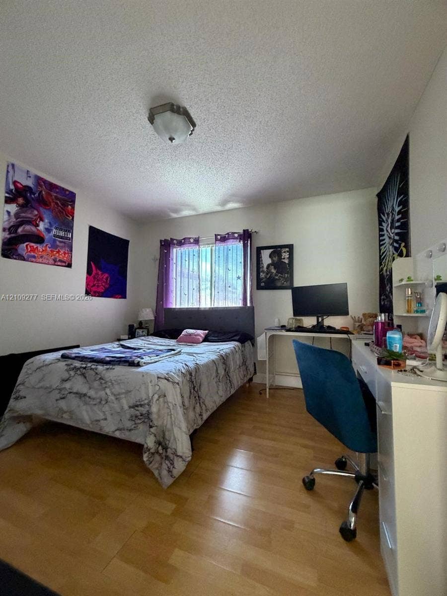 Bedroom featuring wood-finish flooring, a neutral wall palette, a ceiling-mounted light fixture, and a large window with sliding glass panes