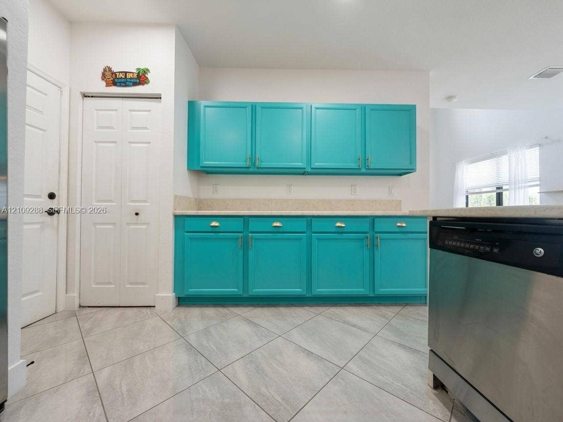Kitchen featuring vibrant blue cabinetry, solid surface countertops, a stainless steel dishwasher, and diagonal-laid tile flooring