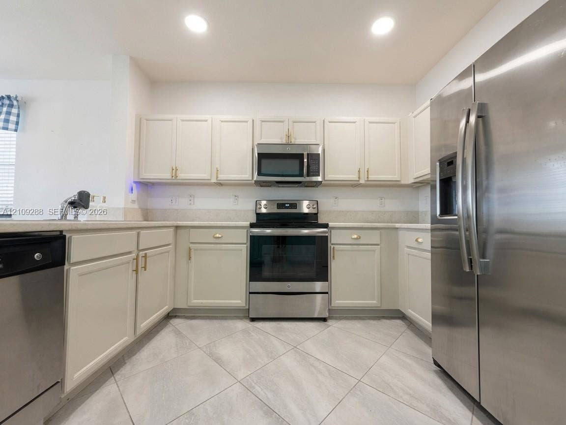 Kitchen featuring off-white cabinetry, stainless steel appliances, neutral countertops, and diagonal tile flooring