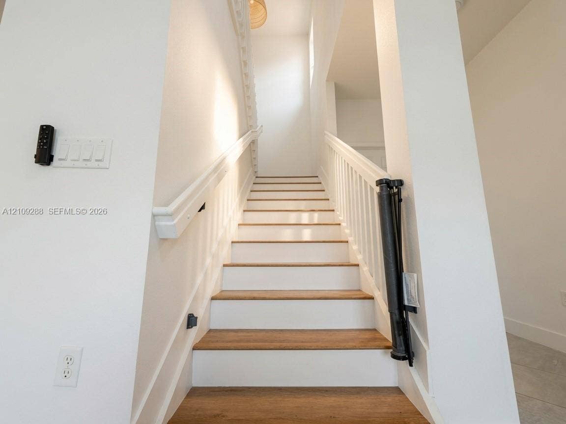 Staircase featuring wood-finish treads, white risers, and a white handrail with vertical balusters