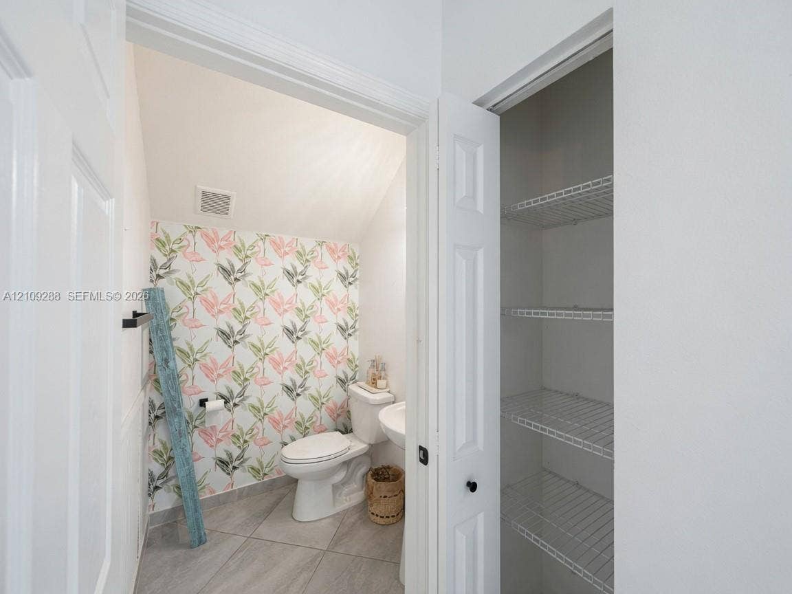 Restroom featuring tile flooring, a pedestal sink, a two-piece toilet, and a built-in closet with wire shelving
