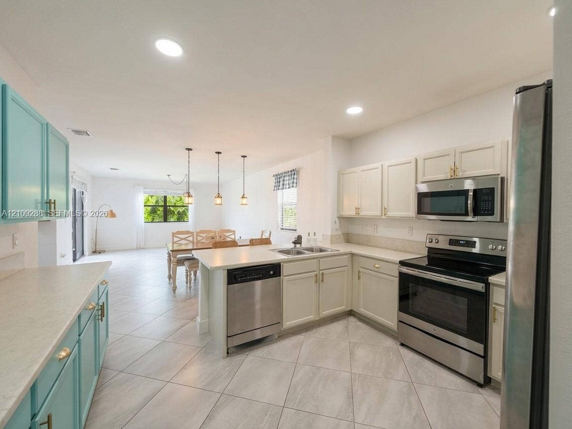 Kitchen featuring light-toned cabinetry, stainless steel appliances, a center island with a built-in dishwasher, neutral countertops, and tile flooring