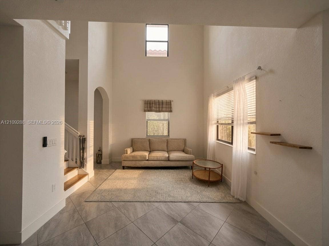 Interior featuring expansive vaulted ceilings, neutral wall tones, large-format tile flooring, a prominent arched architectural detail, and custom wall-mounted shelving
